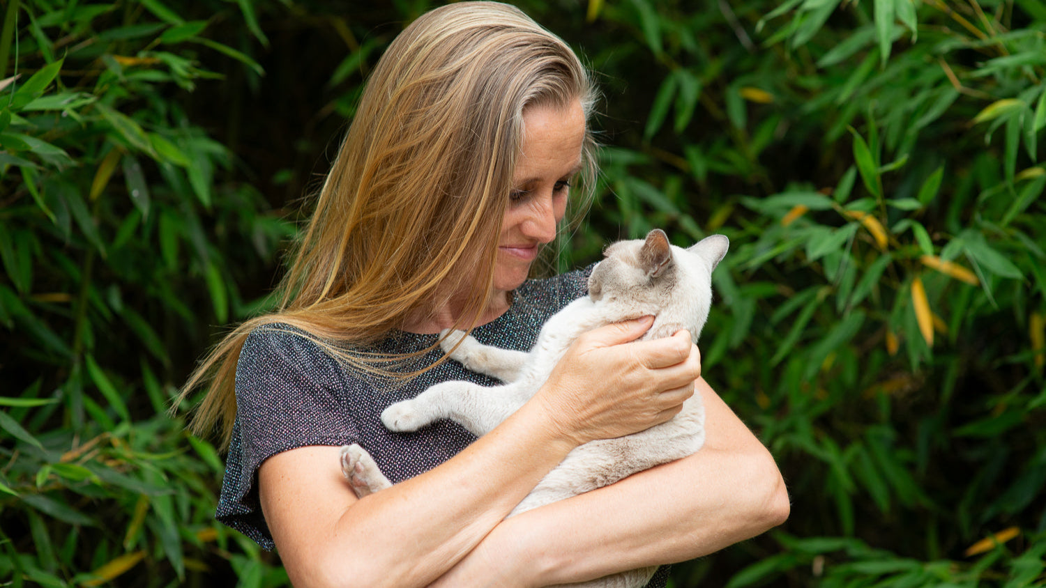 Woman holding a cat against a green leafy background